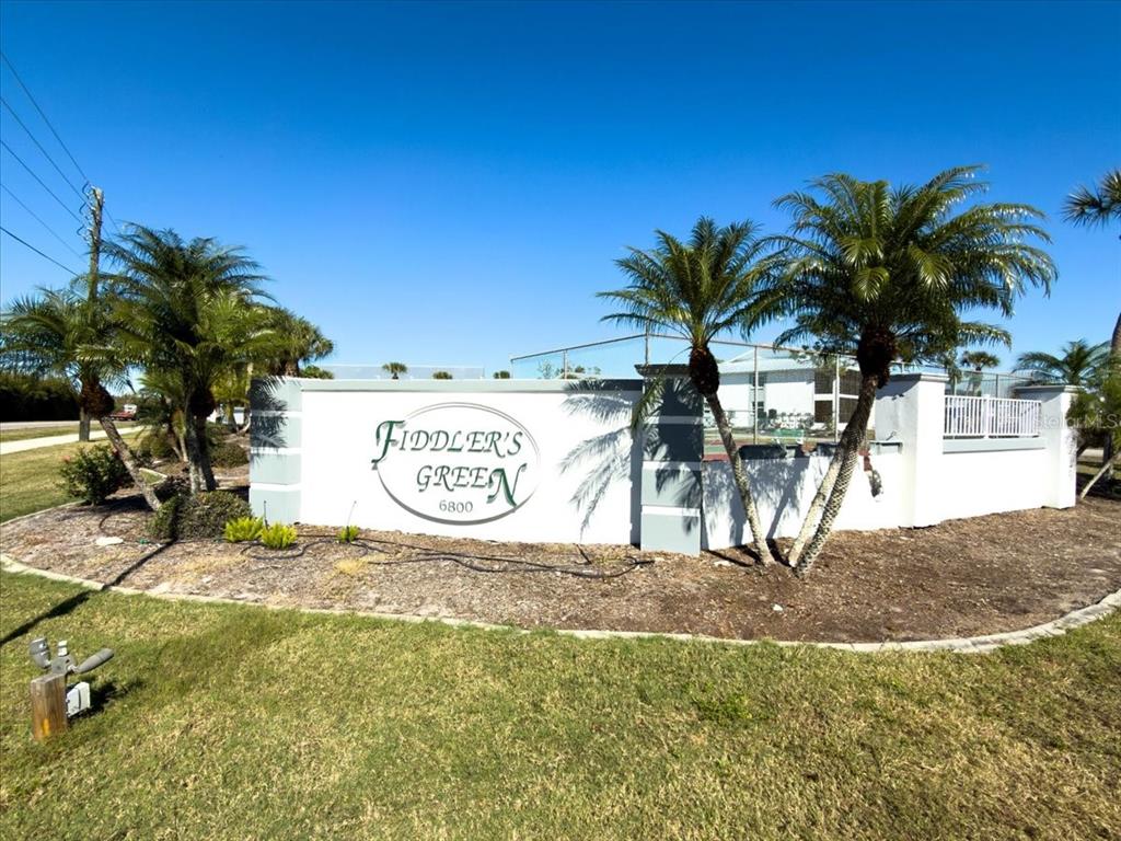 A white monument sign for Fiddler's Green stands in front of palm trees and fencing — 6800 PLACIDA ROAD UNIT 193, ENGLEWOOD, FL