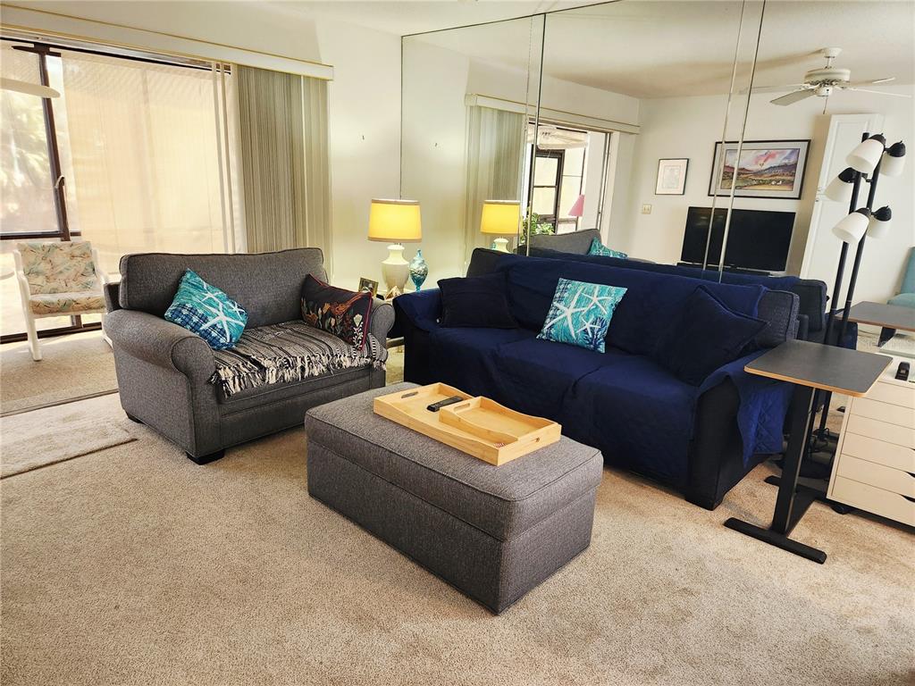 A living room features a gray loveseat, a blue sofa, an ottoman, and mirrored walls — 6800 PLACIDA ROAD UNIT 193, ENGLEWOOD, FL