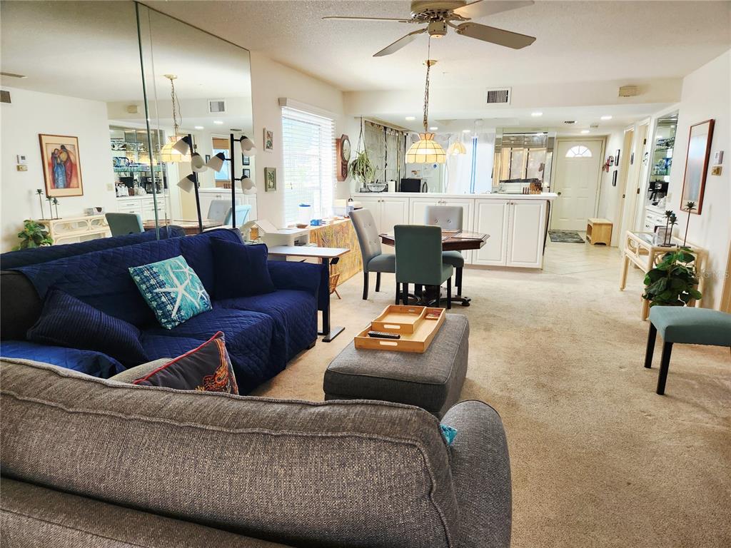 A living room and dining area feature carpeted floors, a blue sofa, and mirrored walls — 6800 PLACIDA ROAD UNIT 193, ENGLEWOOD, FL