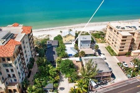 An aerial view shows beachside buildings, a sandy shoreline, and the ocean under a clear sky — 19646 GULF BOULEVARD UNIT 3, INDIAN SHORES, FL