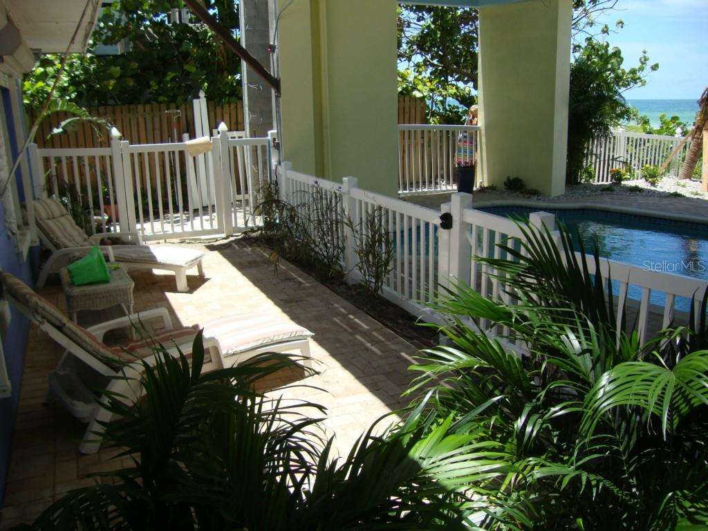 A patio with lounge chairs overlooks a swimming pool and the ocean in the distance — 19646 GULF BOULEVARD UNIT 3, INDIAN SHORES, FL