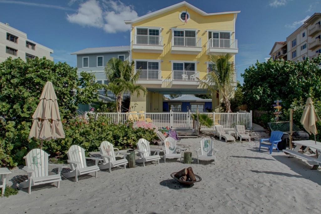A yellow three-story beach house with a sandy backyard, fire pit, and several Adirondack chairs — 19646 GULF BOULEVARD UNIT 3, INDIAN SHORES, FL