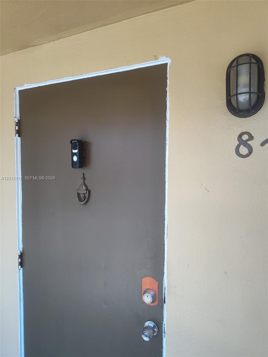 A brown front door with a smart lock and a wall-mounted light fixture — 625 SW 20th Ct # 8A, Delray Beach FL 33445, DELRAY BEACH, FL