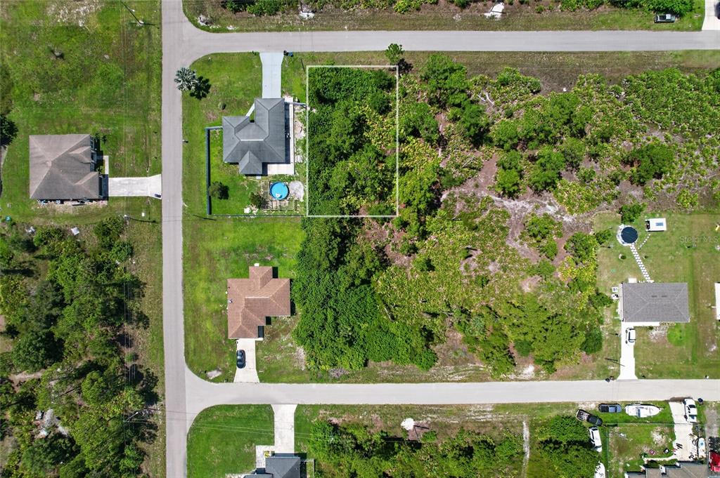 An aerial view shows a vacant, wooded residential lot outlined in white between two houses — 1141 COVE STREET E, LEHIGH ACRES, FL