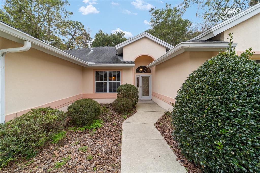 A concrete walkway leads to the front entrance of a peach-colored house with landscaping — 11481 SW 82ND COURT ROAD, OCALA, FL