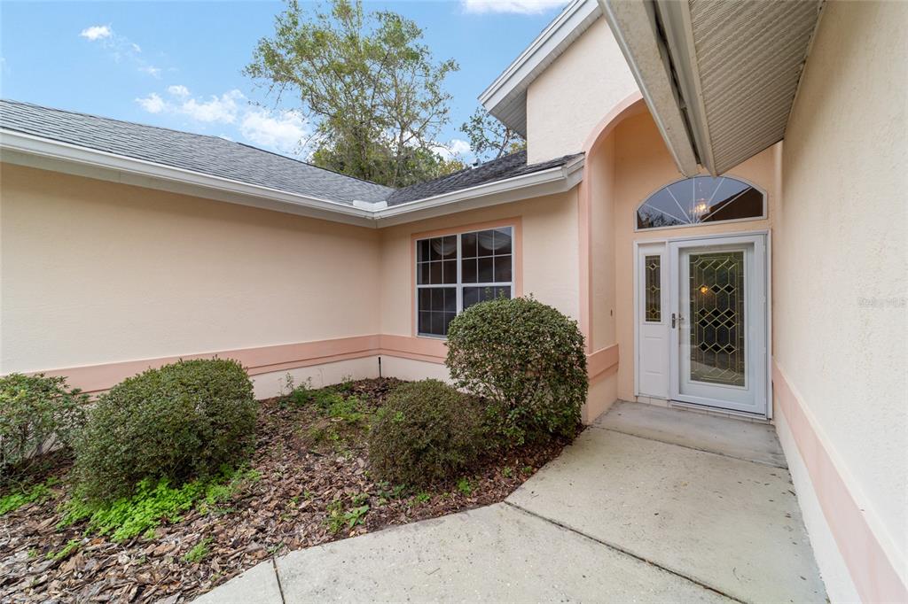 The exterior of a house features a peach-colored facade, a front door with glass, and landscaping — 11481 SW 82ND COURT ROAD, OCALA, FL