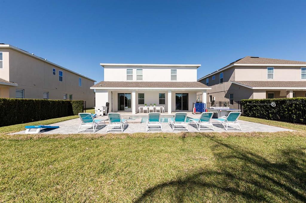 The backyard features a swimming pool, a paved patio with lounge chairs, and a two-story house — 7602 MACKINAW LANE, KISSIMMEE, FL