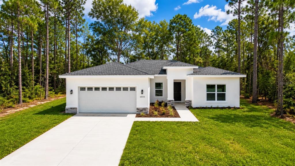 A single-story white house with a two-car garage sits on a grassy lot — 6805 SW 131ST PLACE, OCALA, FL