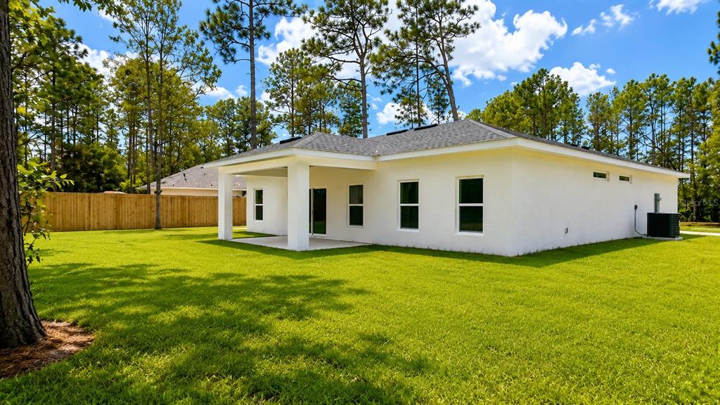 The exterior rear view of a white stucco house features a covered patio and lawn — 6805 SW 131ST PLACE, OCALA, FL