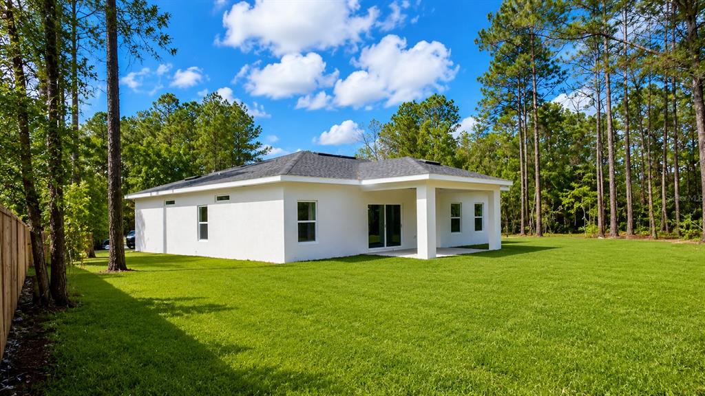 The rear exterior of a white stucco house features a covered patio and grassy yard — 6805 SW 131ST PLACE, OCALA, FL
