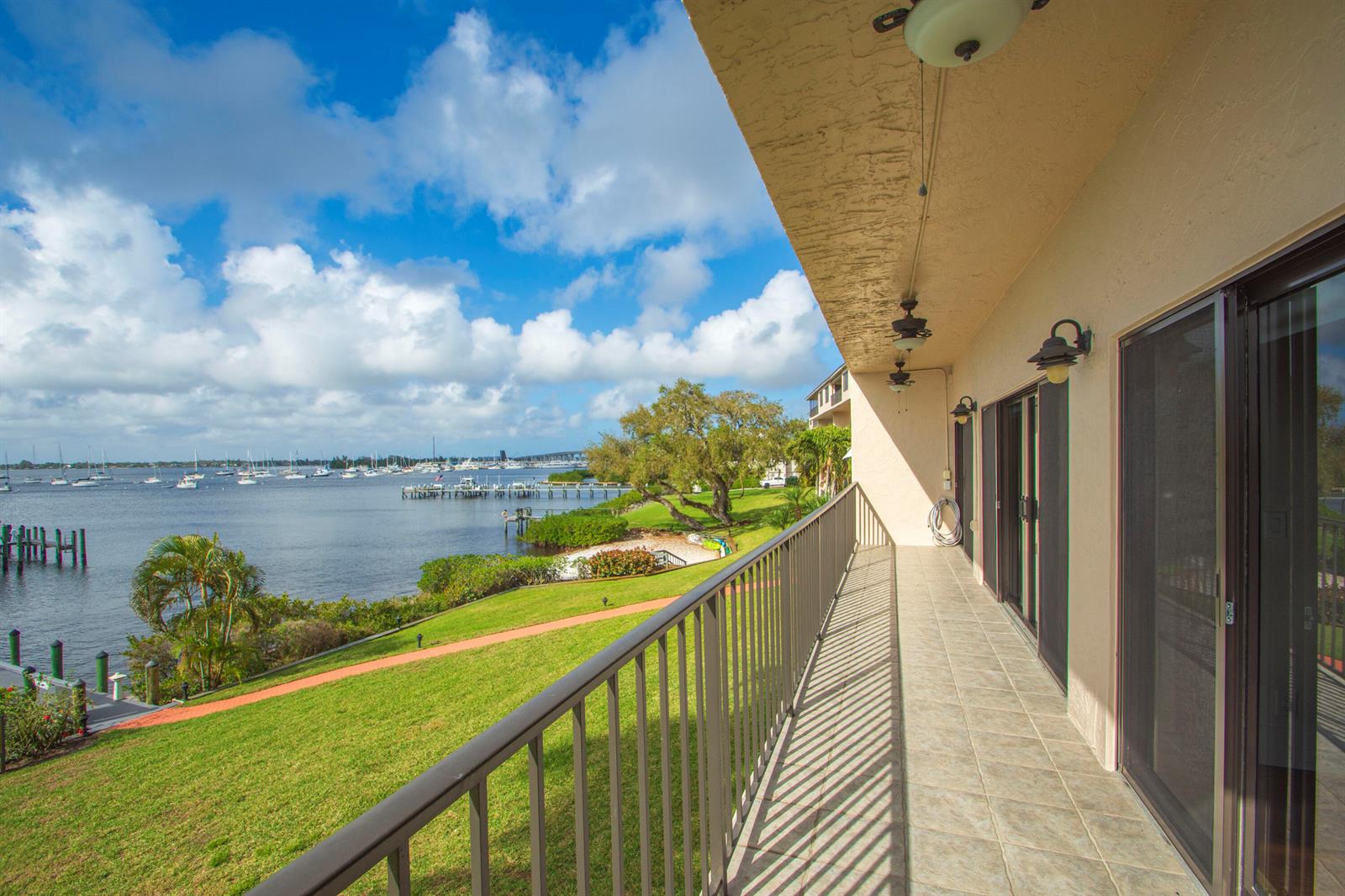 A balcony with a metal railing overlooks a grassy lawn, trees, and a boat-filled bay — 624 SW St. Lucie Crescent # 206, Stuart FL 34994, STUART, FL