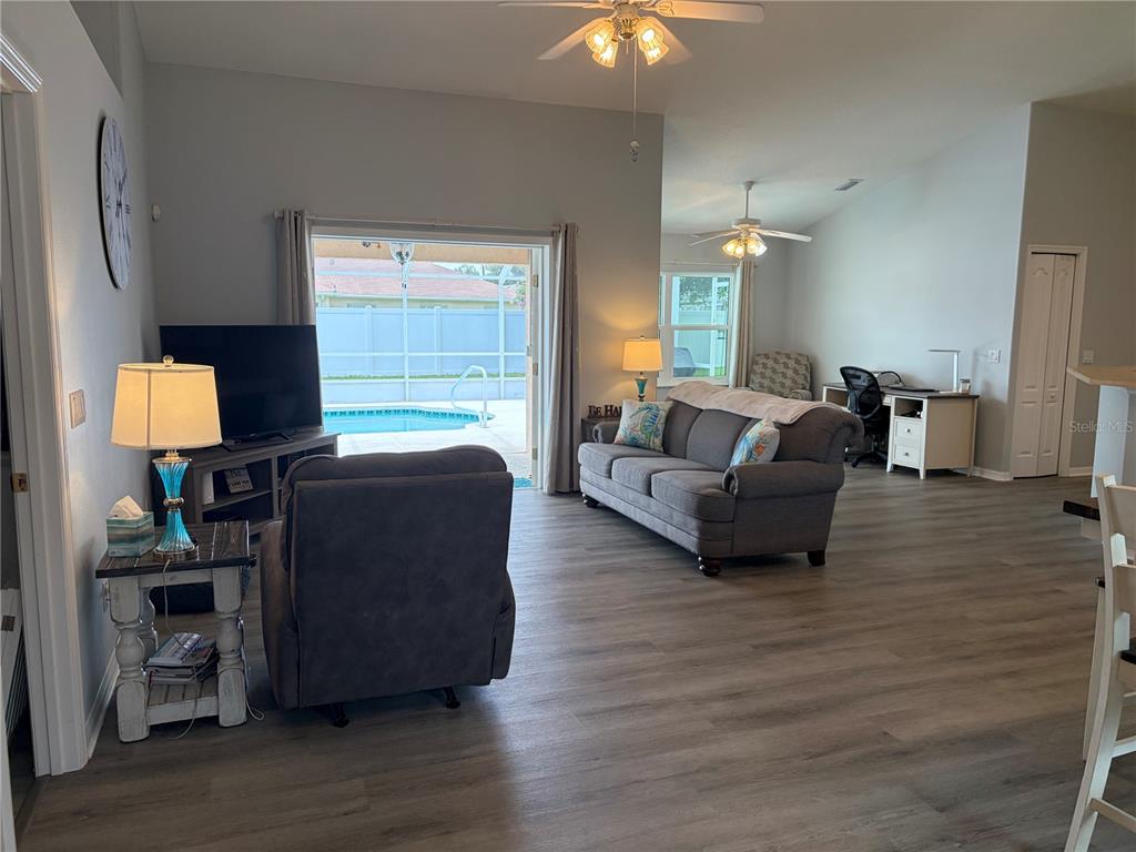 A living room with gray wood-look flooring, a sofa, a recliner, and a pool view — 25 BISCAY LANE, PALM COAST, FL