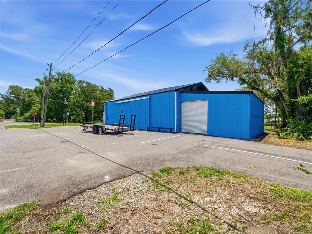 A bright blue metal warehouse building sits on an asphalt lot with a trailer parked outside — 490 SMITH STREET, BROOKSVILLE, FL