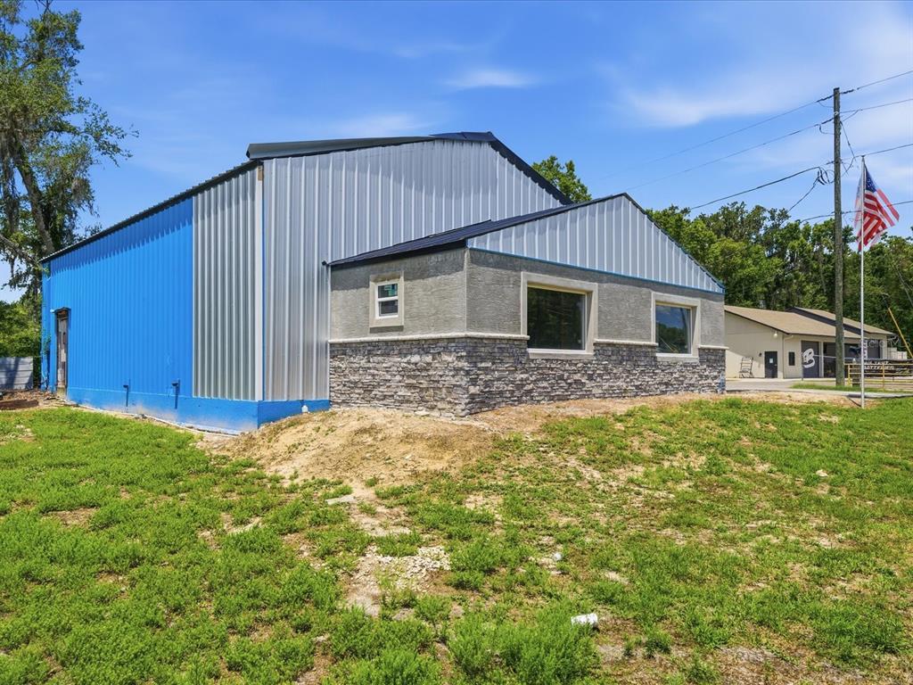 A metal-sided building with a stone-accented facade stands on a grassy lot under blue skies — 490 SMITH STREET, BROOKSVILLE, FL