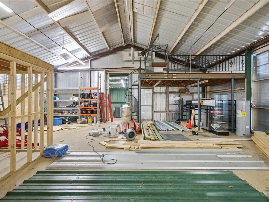 An interior view of a large industrial workshop featuring a loft, spiral staircase, and construction materials — 490 SMITH STREET, BROOKSVILLE, FL
