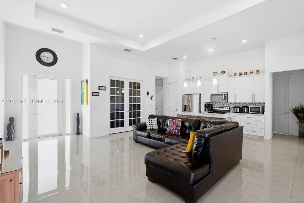 An open-concept living room features a black leather sectional, white kitchen cabinetry, and tile flooring — 1211 Eclat St E, Lehigh Acres FL 33974, LEHIGH ACRES, FL