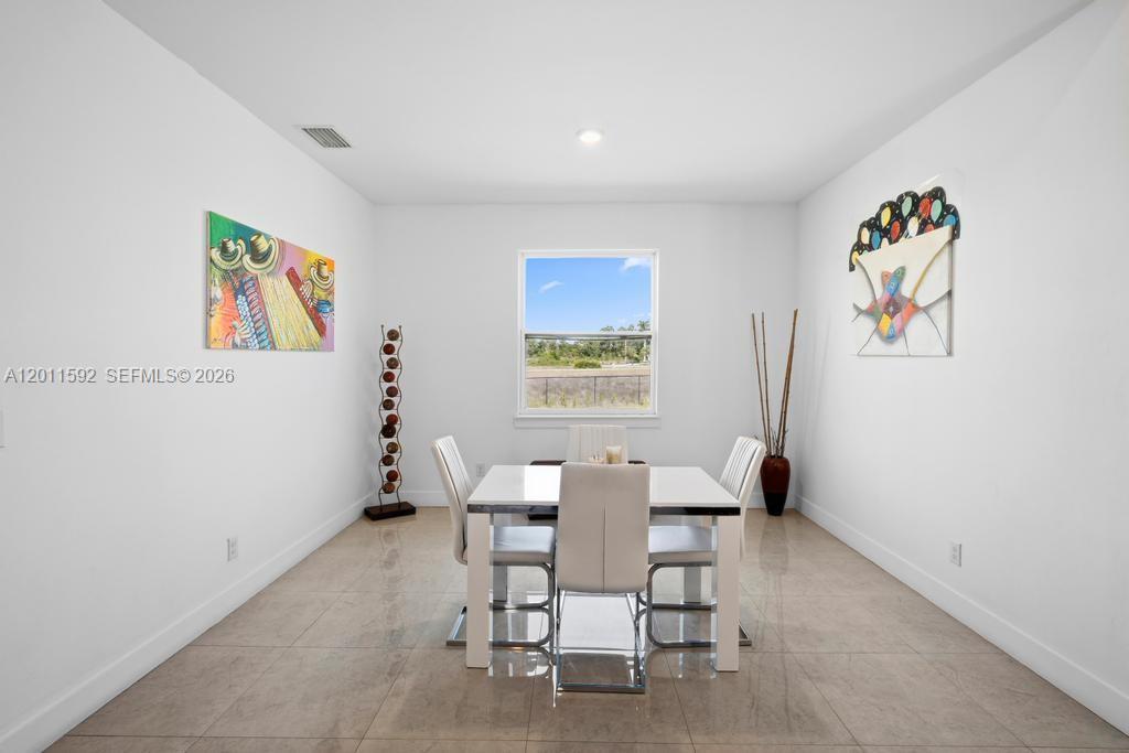 A dining room features a white table, four chairs, tile flooring, and two wall paintings — 1211 Eclat St E, Lehigh Acres FL 33974, LEHIGH ACRES, FL
