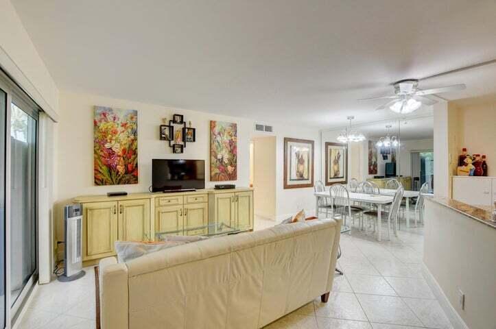 A living room with a beige sofa, light-colored cabinets, a television, and a dining area — 7539 S Oriole Boulevard # 103, Delray Beach FL 33446, DELRAY BEACH, FL