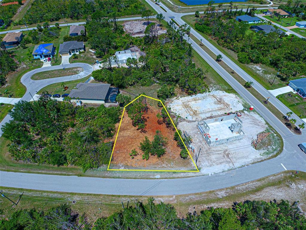 An aerial view shows a vacant, trapezoidal residential lot outlined in yellow near a construction site — 116 REDWOOD ROAD, ROTONDA WEST, FL