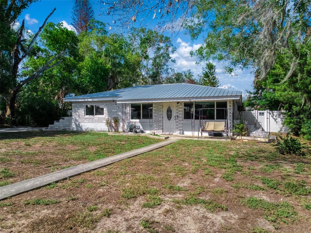 A single-story house with a metal roof and white brick exterior sits on a grassy lot — 1018 BELLEVUE AVENUE, SEBRING, FL