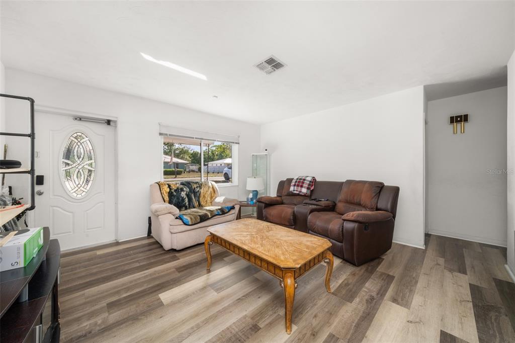 A living room features wood-look flooring, a brown leather sofa, a beige armchair, and a coffee table — 1018 BELLEVUE AVENUE, SEBRING, FL