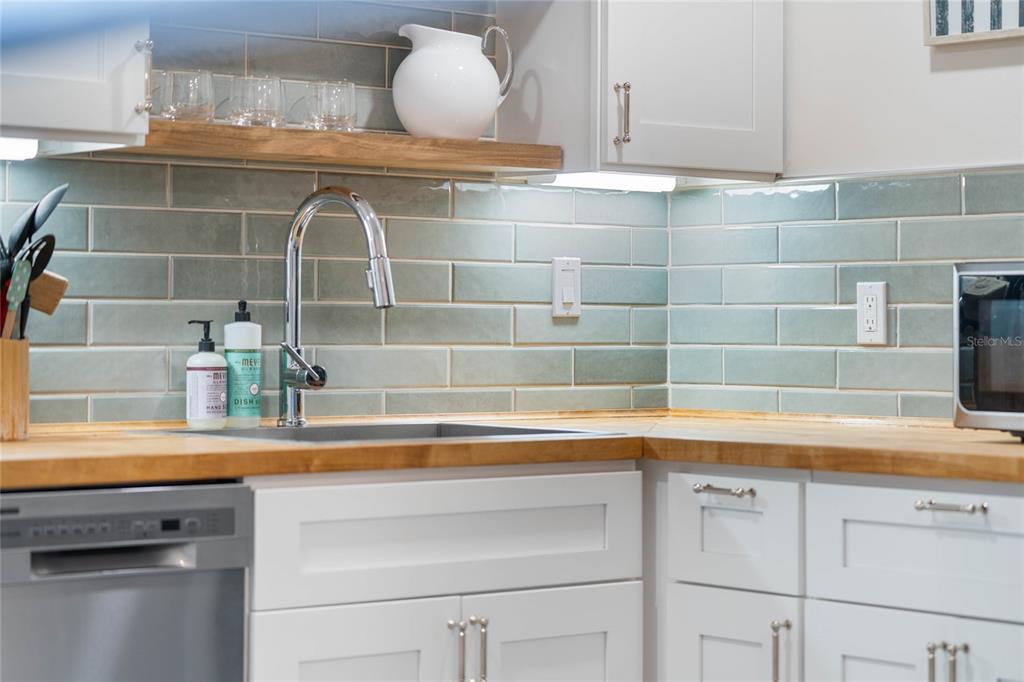 A kitchen sink area features light blue subway tile, wood countertops, and white cabinetry — 1409 SOUTHARD AVENUE, NEW SMYRNA BEACH, FL