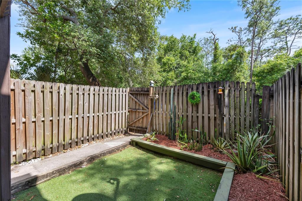 A fenced-in backyard features artificial turf, a raised garden bed with cacti, and a gate — 1329 WINDSOR DRIVE, KISSIMMEE, FL