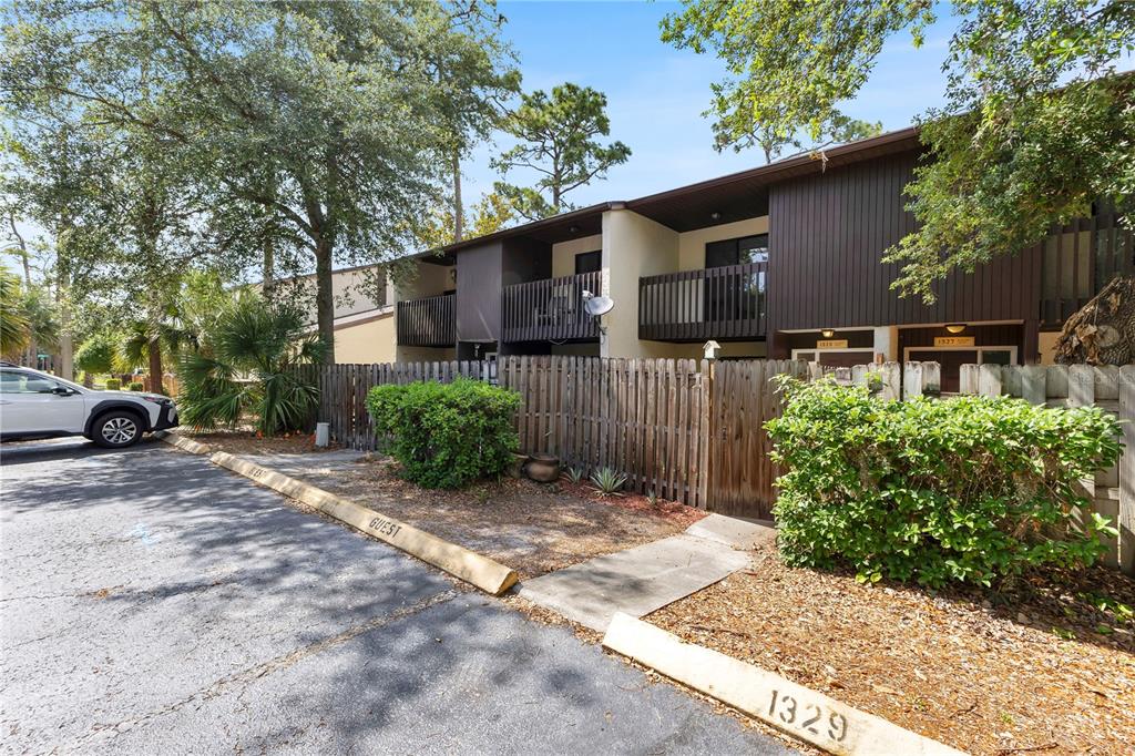 A two-story apartment building exterior with balconies, a wooden fence, and marked parking spaces — 1329 WINDSOR DRIVE, KISSIMMEE, FL