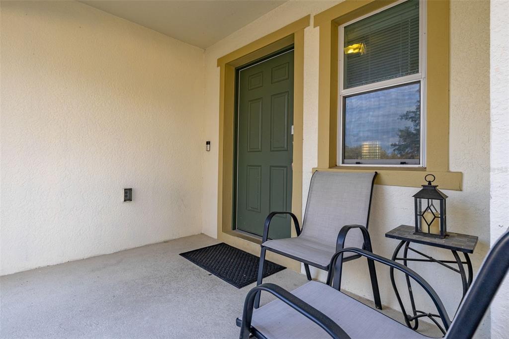 A covered porch features a green front door, a window, and two outdoor chairs — 947 EMERALD GREEN COURT, KISSIMMEE, FL