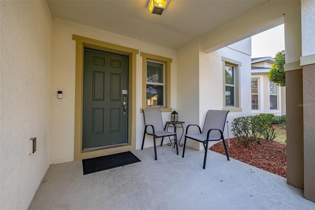 A covered front porch features a green door, two chairs, and a small side table — 947 EMERALD GREEN COURT, KISSIMMEE, FL