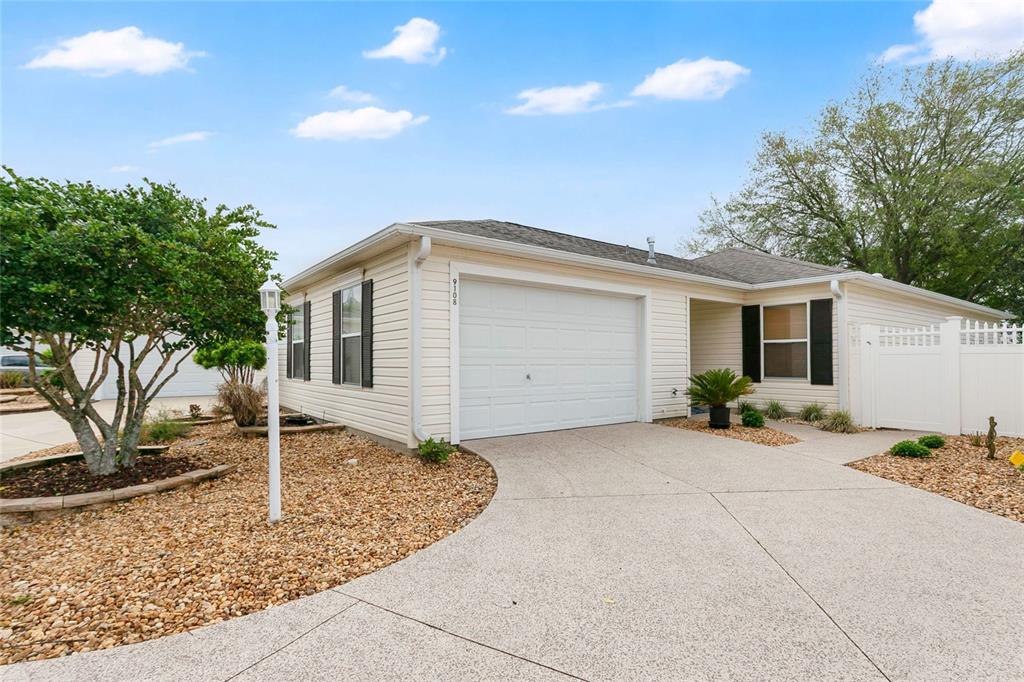 A single-story house with beige siding, a white garage door, and a gravel front yard — 9108 SE 177TH BELMONT PLACE, THE VILLAGES, FL