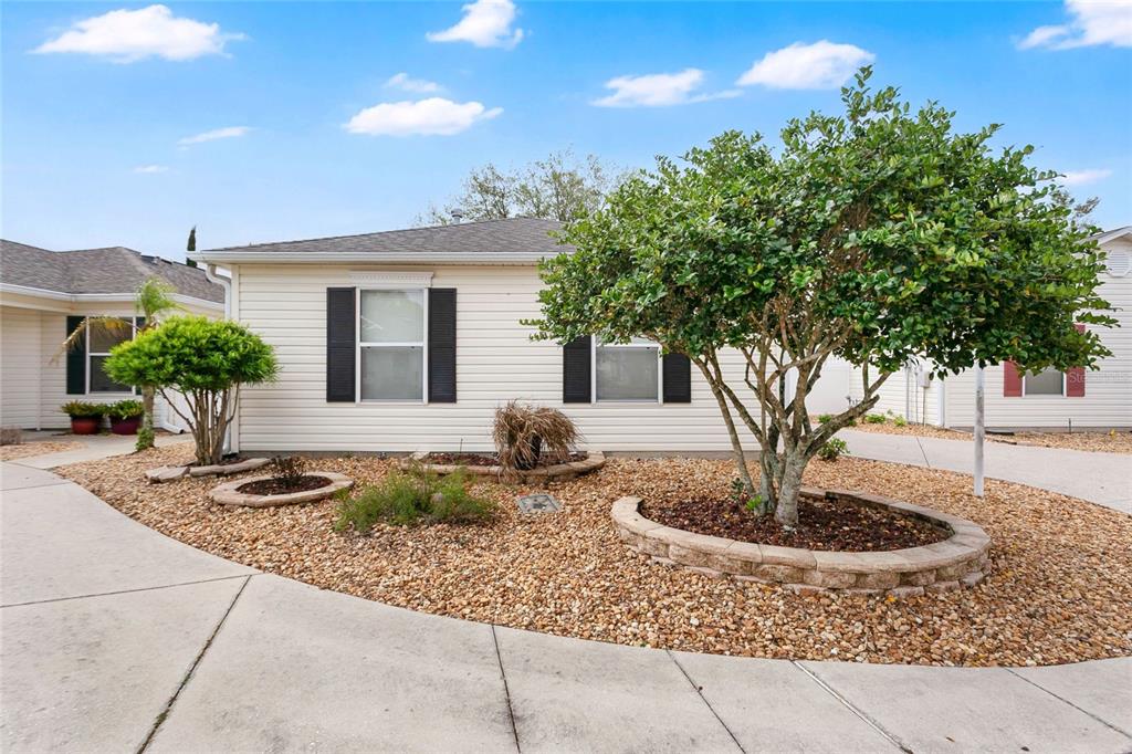 A single-story house with light siding, black shutters, and a landscaped front yard with trees — 9108 SE 177TH BELMONT PLACE, THE VILLAGES, FL