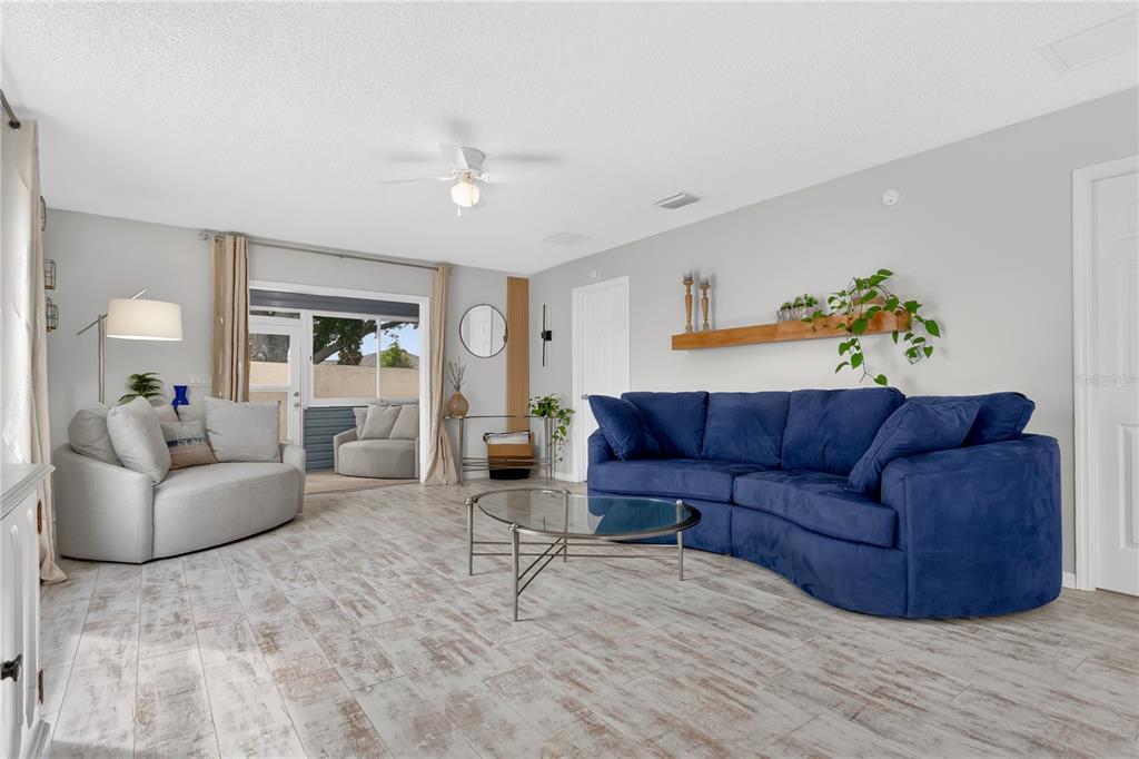 A living room features a blue curved sofa, light wood-look tile floors, and a glass table — 9108 SE 177TH BELMONT PLACE, THE VILLAGES, FL