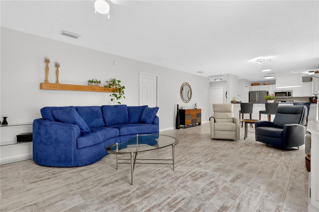 A living room with a blue sectional sofa, two armchairs, and light wood-look tile flooring — 9108 SE 177TH BELMONT PLACE, THE VILLAGES, FL