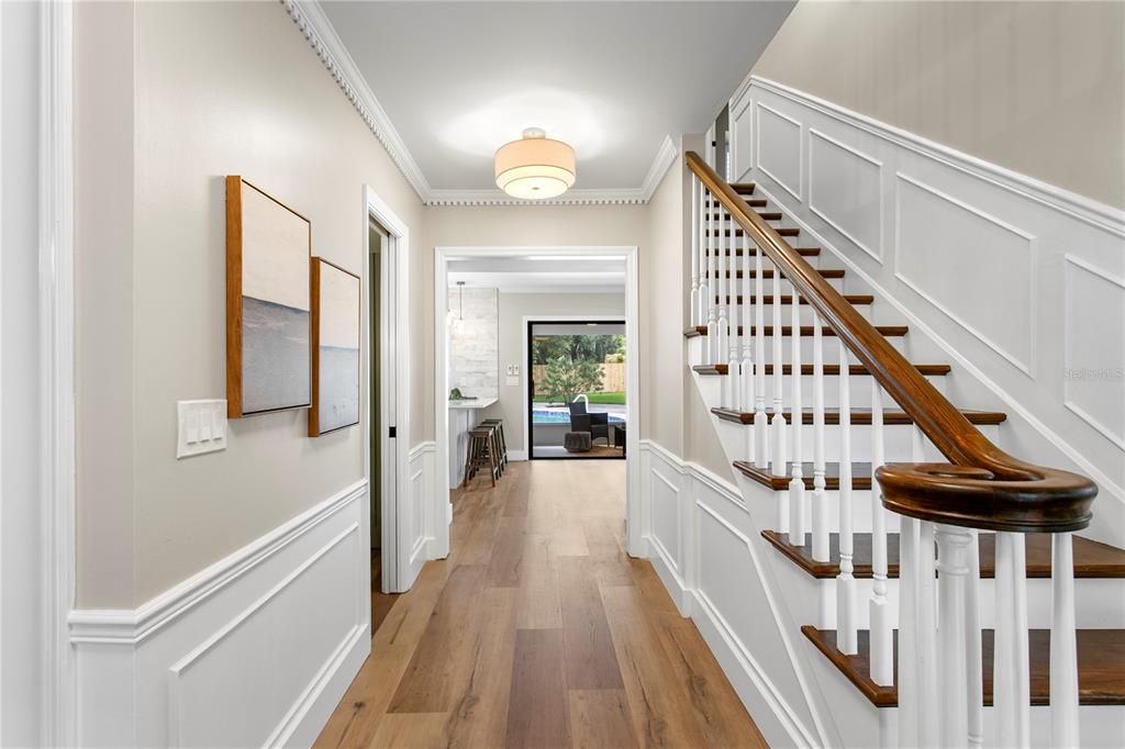 A hallway with wood floors, white wainscoting, and a staircase leads to a backyard view — 13305 GOLF CREST CIRCLE, TAMPA, FL