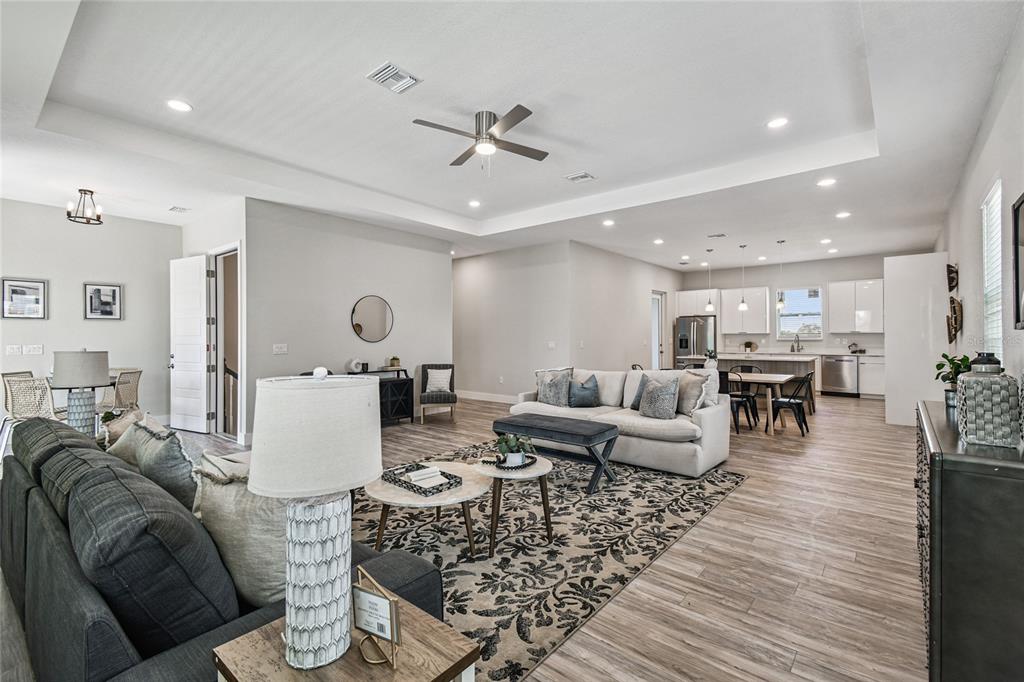 An open-concept living room and kitchen feature light wood-look flooring and a tray ceiling — 4559 MITCHER ROAD, NEW PORT RICHEY, FL