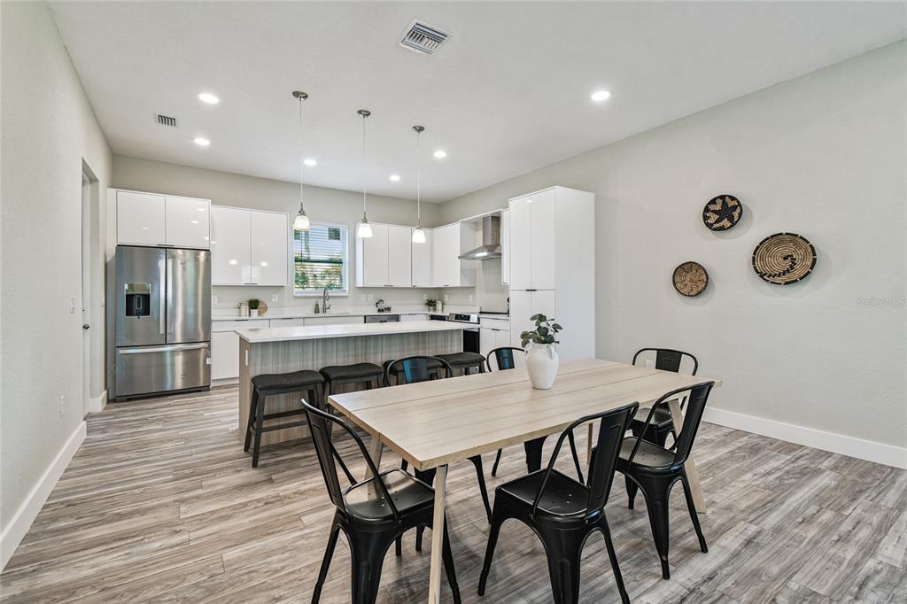 A modern kitchen features white cabinetry, stainless steel appliances, a breakfast bar, and a dining area — 4559 MITCHER ROAD, NEW PORT RICHEY, FL