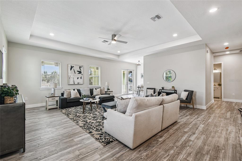 A spacious living room features a tray ceiling, light wood-look flooring, and neutral furniture — 4559 MITCHER ROAD, NEW PORT RICHEY, FL