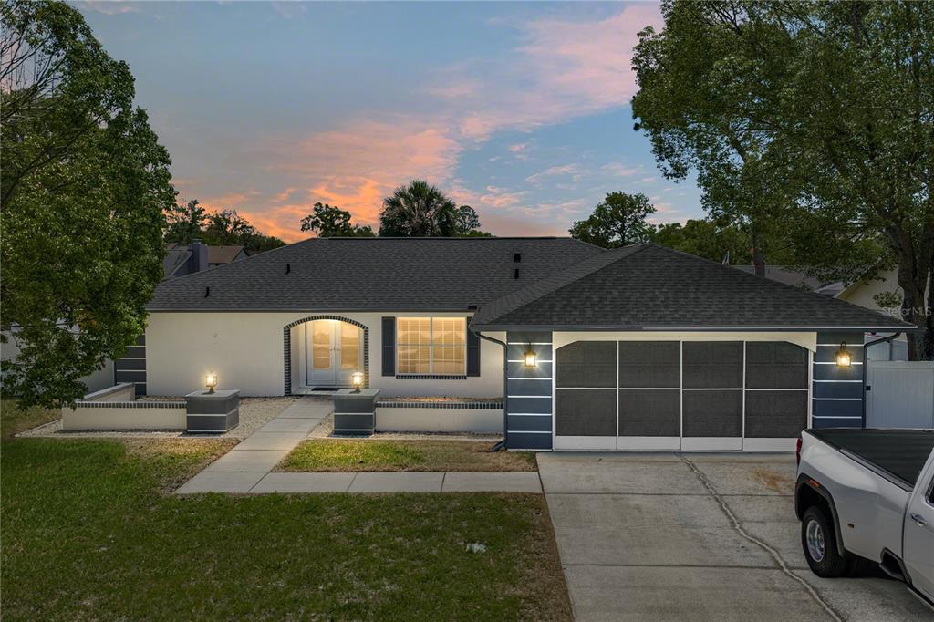 A single-story house with a white stucco exterior, dark roof, and a screened-in garage door — 7435 KILBRIDE COURT, WEEKI WACHEE, FL