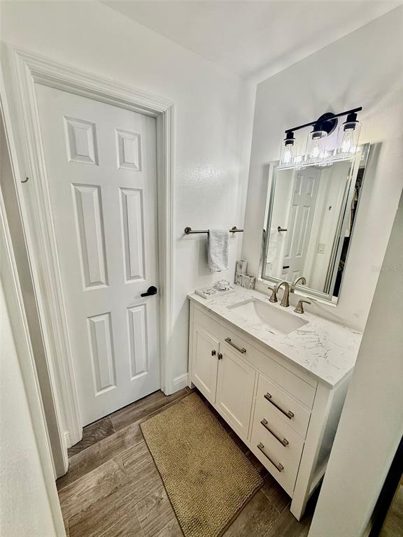 A bathroom features a white vanity with a marble countertop, a mirror, and wood-look flooring — 300 PROMENADE DRIVE UNIT 105, DUNEDIN, FL