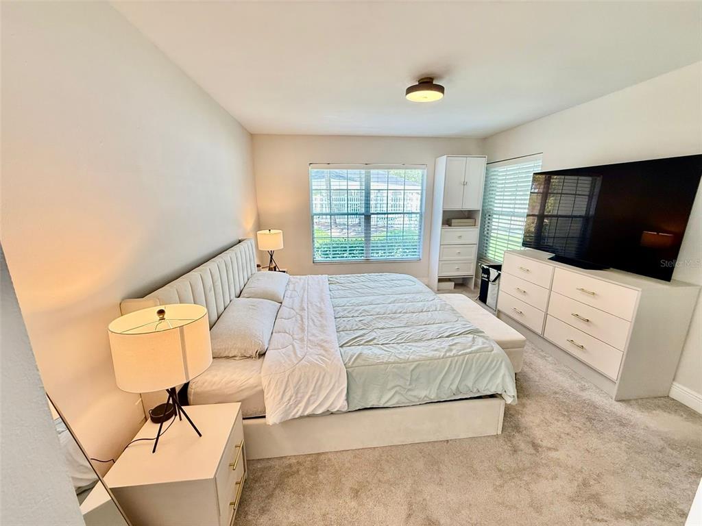 A bedroom features a bed with a tufted headboard, a dresser, and a large television — 300 PROMENADE DRIVE UNIT 105, DUNEDIN, FL