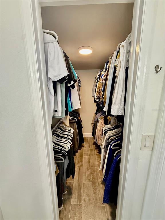 A walk-in closet with hanging clothes on both sides and wood-look tile flooring — 300 PROMENADE DRIVE UNIT 105, DUNEDIN, FL