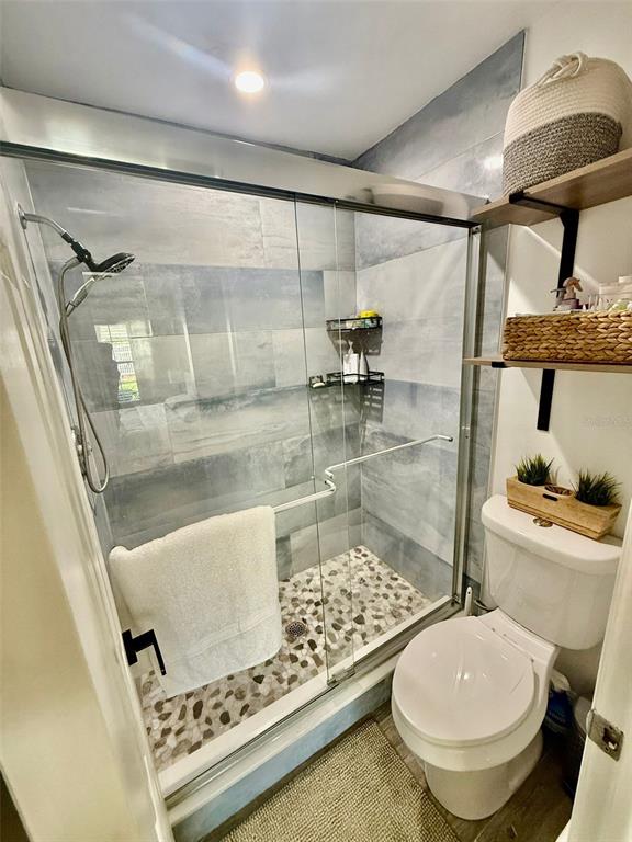 A bathroom features a glass-enclosed shower with pebble flooring and a white toilet — 300 PROMENADE DRIVE UNIT 105, DUNEDIN, FL