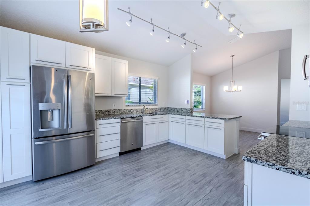 A kitchen with white cabinets, stainless steel appliances, granite countertops, and gray wood-look flooring — 3667 KINGSWOOD COURT, CLERMONT, FL
