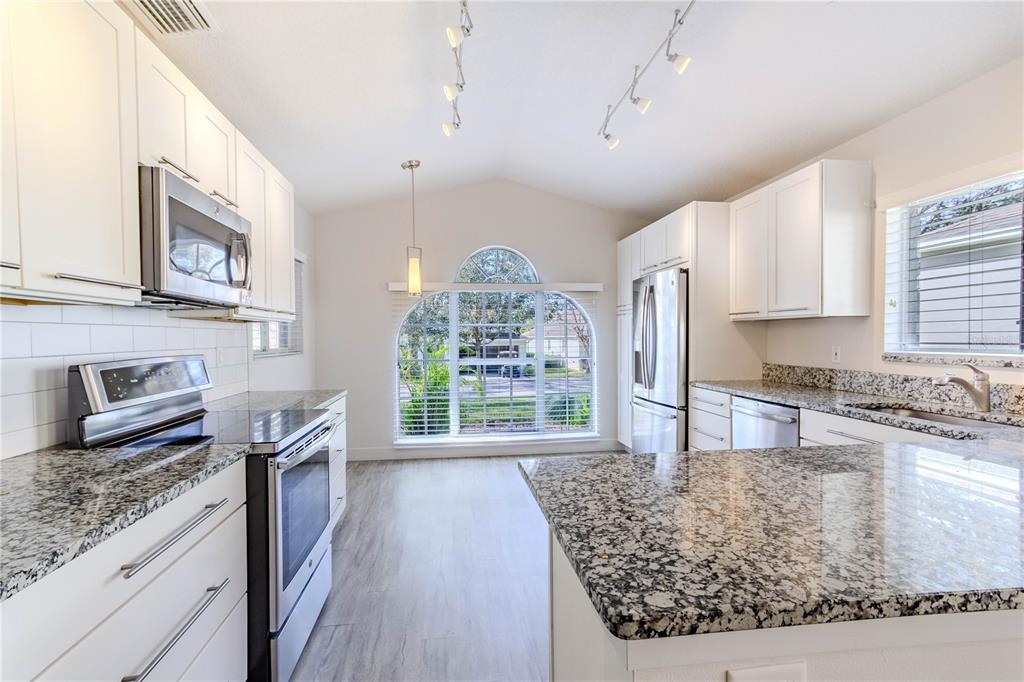 A kitchen with white cabinets, granite countertops, stainless steel appliances, and a large arched window — 3667 KINGSWOOD COURT, CLERMONT, FL