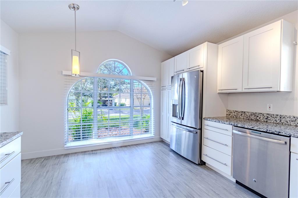 A kitchen features white cabinets, granite countertops, stainless steel appliances, and a large arched window — 3667 KINGSWOOD COURT, CLERMONT, FL