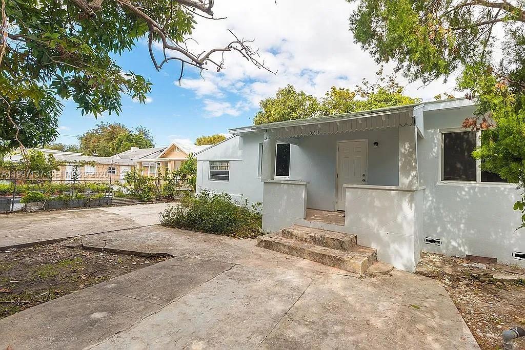 A light blue single-story house with a concrete porch and driveway under a cloudy sky — 361 NE 57th St, Miami FL 33137, MIAMI, FL
