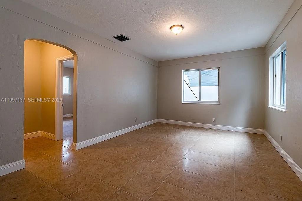 An empty room features beige walls, light-colored tile flooring, and two windows — 361 NE 57th St, Miami FL 33137, MIAMI, FL
