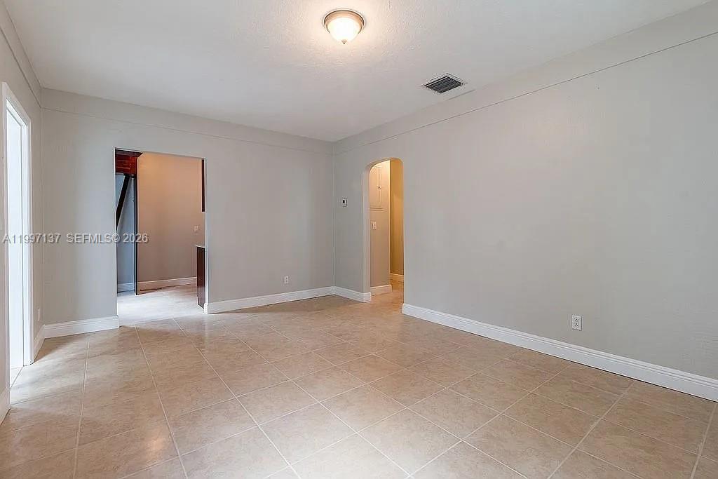 An empty room features light-colored tile flooring, neutral gray walls, and two arched doorways — 361 NE 57th St, Miami FL 33137, MIAMI, FL