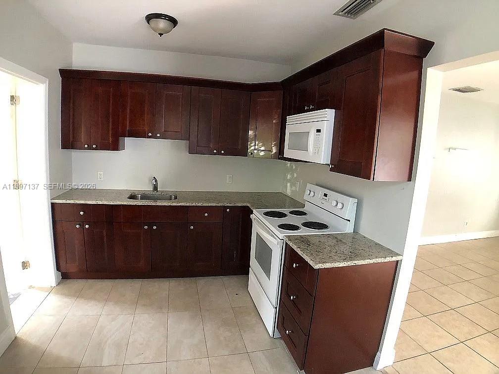 A kitchen features dark wood cabinets, granite countertops, and white appliances — 361 NE 57th St, Miami FL 33137, MIAMI, FL